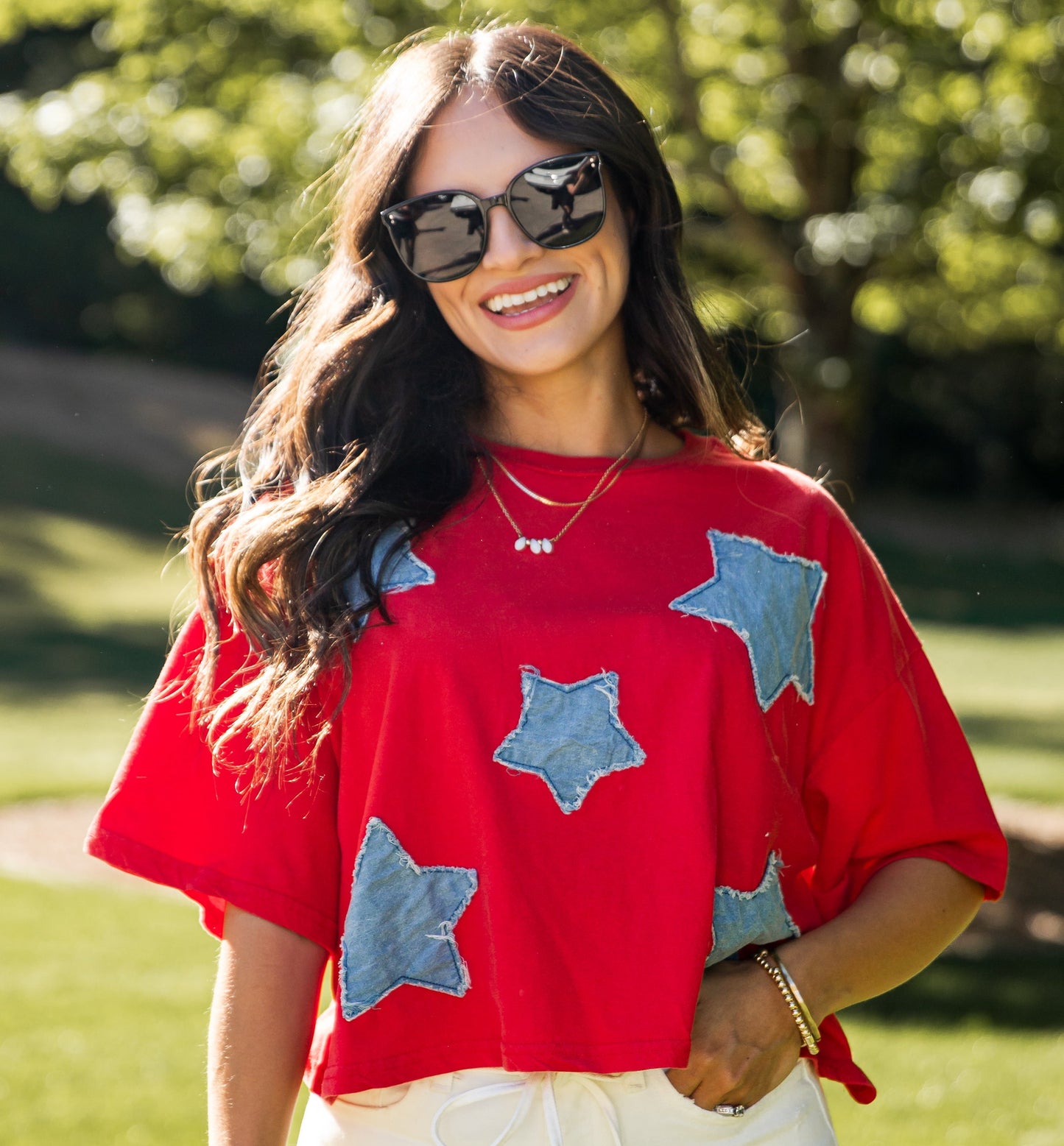 Woman wearing a red shirt with blue star patterns and white shorts outdoors.