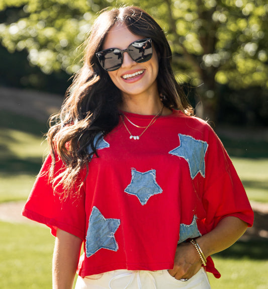 Woman wearing a red shirt with blue star patterns and white shorts outdoors.